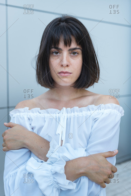 Serious female in trendy blouse crossing hands and looking at camera against gray wall outside building