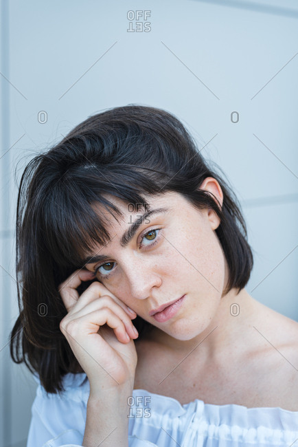 Woman in trendy blouse touching hair and looking at camera against gray wall outside building