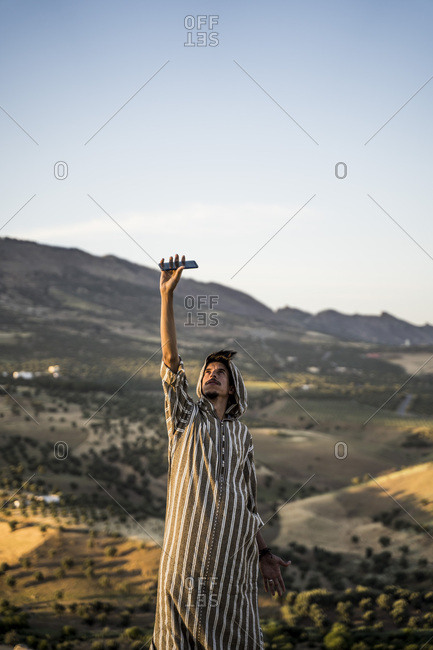 Moroccan man in typical Arabic attire lifting mobile phone up.