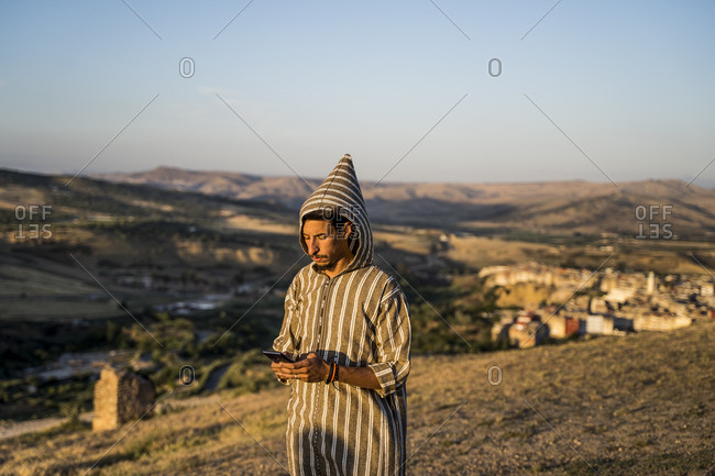 Moroccan man in typical Arabic attire with mobile phone in hand.