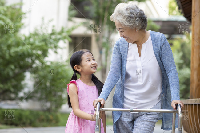 Senior Chinese woman walking with walking frame under granddaughter's assistance