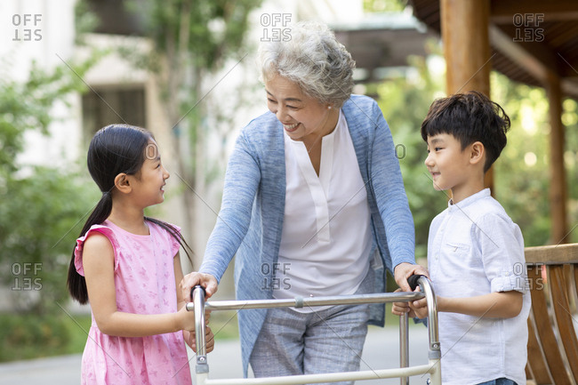 Happy Chinese sibling helping grandma walking with walking frame