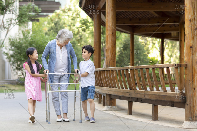 Happy Chinese sibling helping grandma walking with walking frame