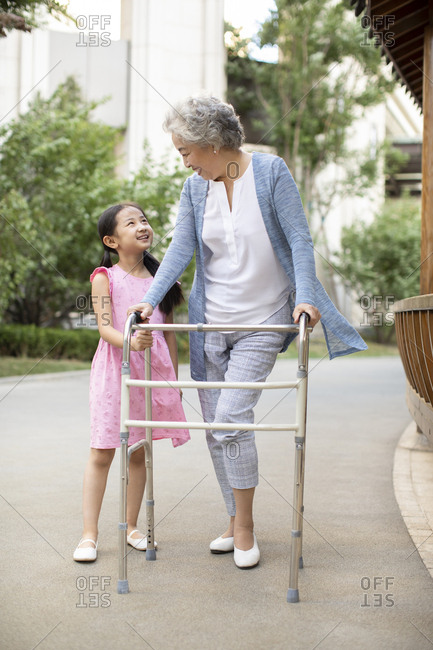 Senior Chinese woman walking with walking frame under granddaughter's assistance