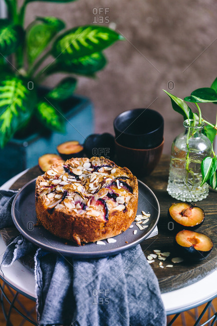 Plum cake with almonds on a plate beside a plant