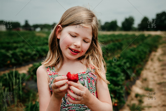 Girl with messy face eating a freshly picked strawberry in a garden