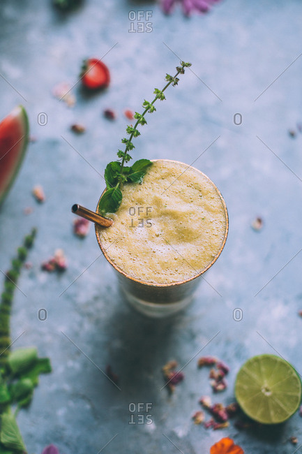 Green cocktail with foam and basil sprig.