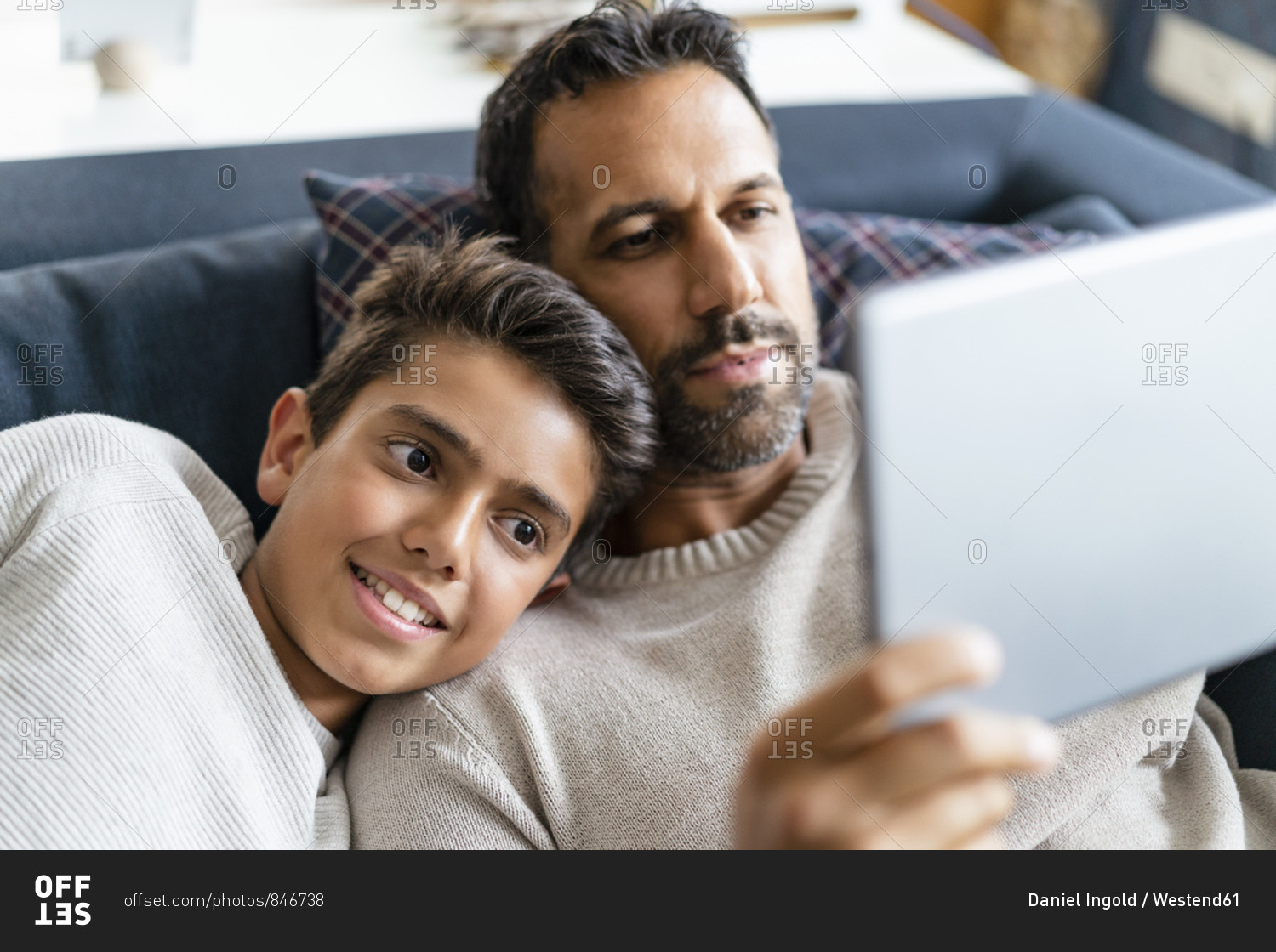 Happy father and son using tablet on couch in living room