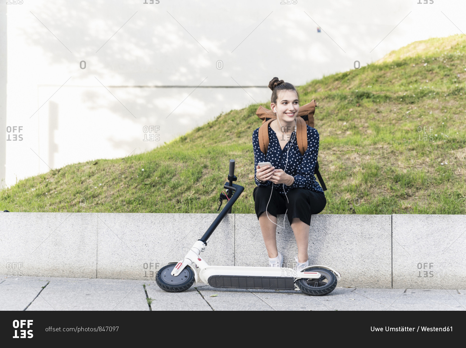 Smiling young woman with electric scooter- earphones and cell phone ...