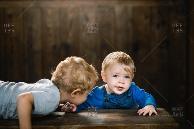 Brother leaning in to baby brother on wooden bench