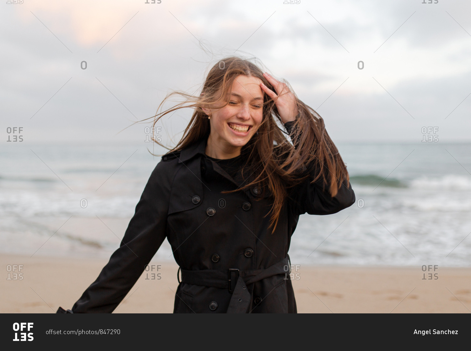Portrait of young woman with hat and trench coat on the beach in a cloudy day of winter