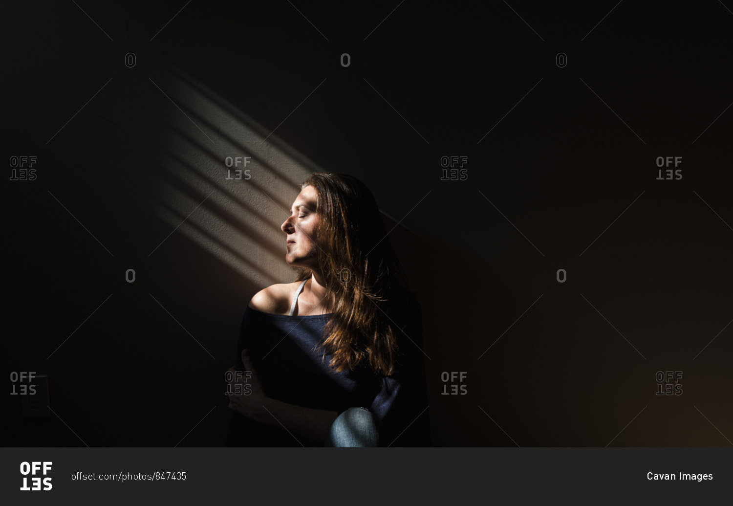 Profile of a woman sitting in a patch of light in a darkened room.