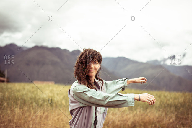 Girl with wild curly hair spins and smiles in field with mountains