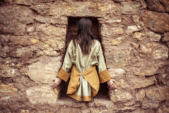 dancer with high fashion jackets sits in key hole in stone wall