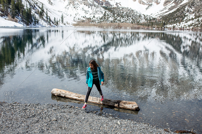 Girl steps off a large log floating in a partially frozen lake