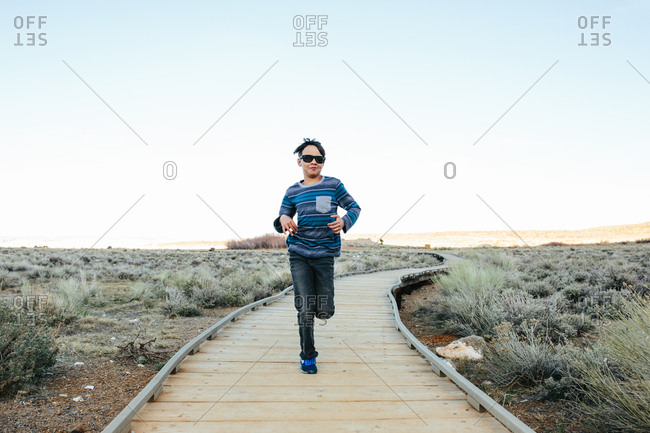 Boy wearing sunglasses runs toward camera on a boardwalk