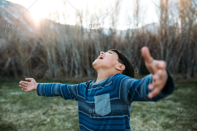 Boy outside with arms wide joyfully yells toward the sky
