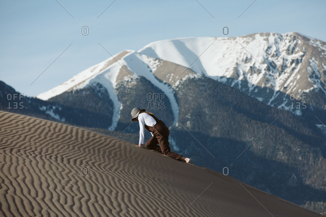 Tired wanderer climbs on hands and knees up sand dune