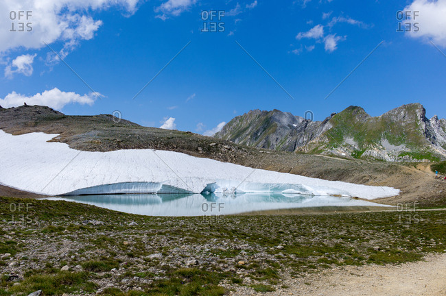 Pile of snow lining lake, melting in the sun on a mountain in Northern Europe