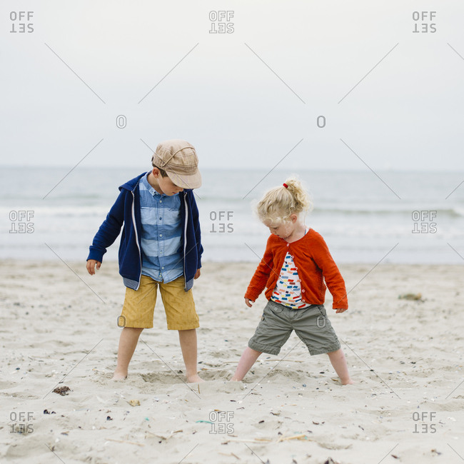 Brother and sister play with feet in the sand on a beach of northern Europe