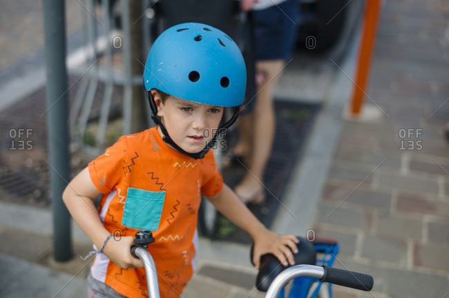 Young boy getting ready to ride his bike with a blue helmet and an orange t-shirt