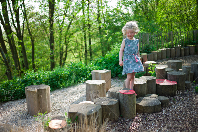 Little girl balancing, on colored wooden logs in a forest path