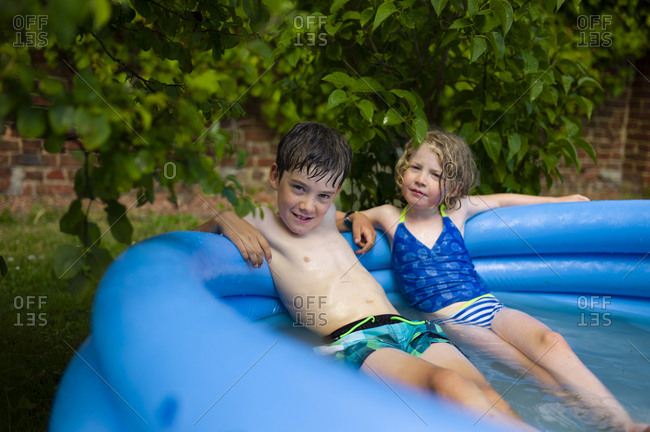 Brother and a sister sitting in the shade in an inflatable pool on a hot summer day