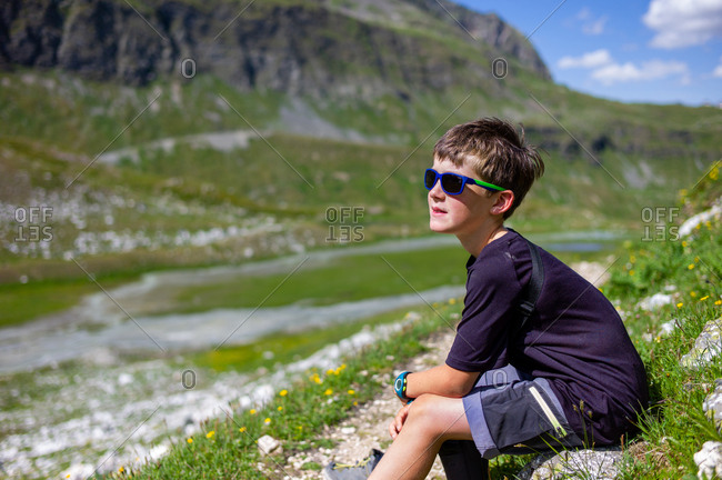 Young boy taking a break and looking at the green and mineral landscape during a hike