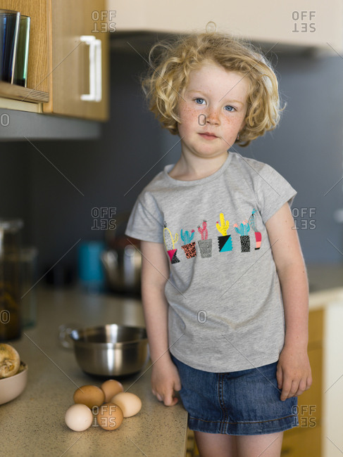 Little girl standing in kitchen ready to cook a cake with eggs and a stainless steel bowl