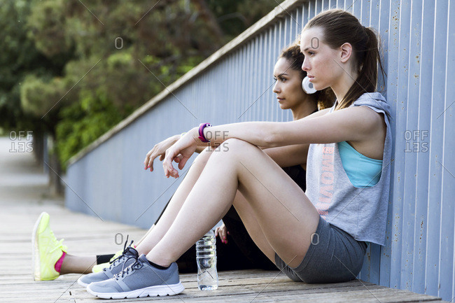 Two sporty young women relaxing on a bridge after workout