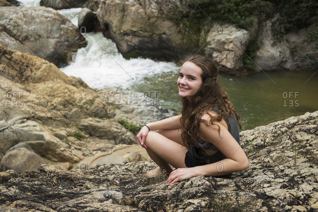 A teenage girl sitting on a rock with a waterfall in the background in Yalepa, Jalisco, Mexico