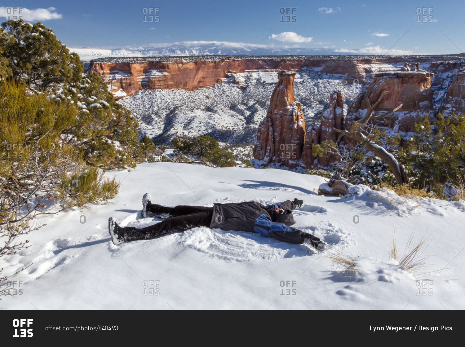 A woman makes a snow angel in the snow in front of the Colorado National Monument
