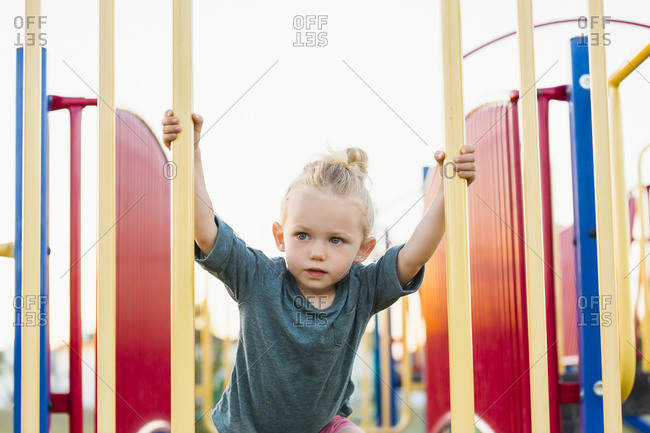 A young girl with blond hair playing in a playground and climbing up a rock ladder on a warm fall day