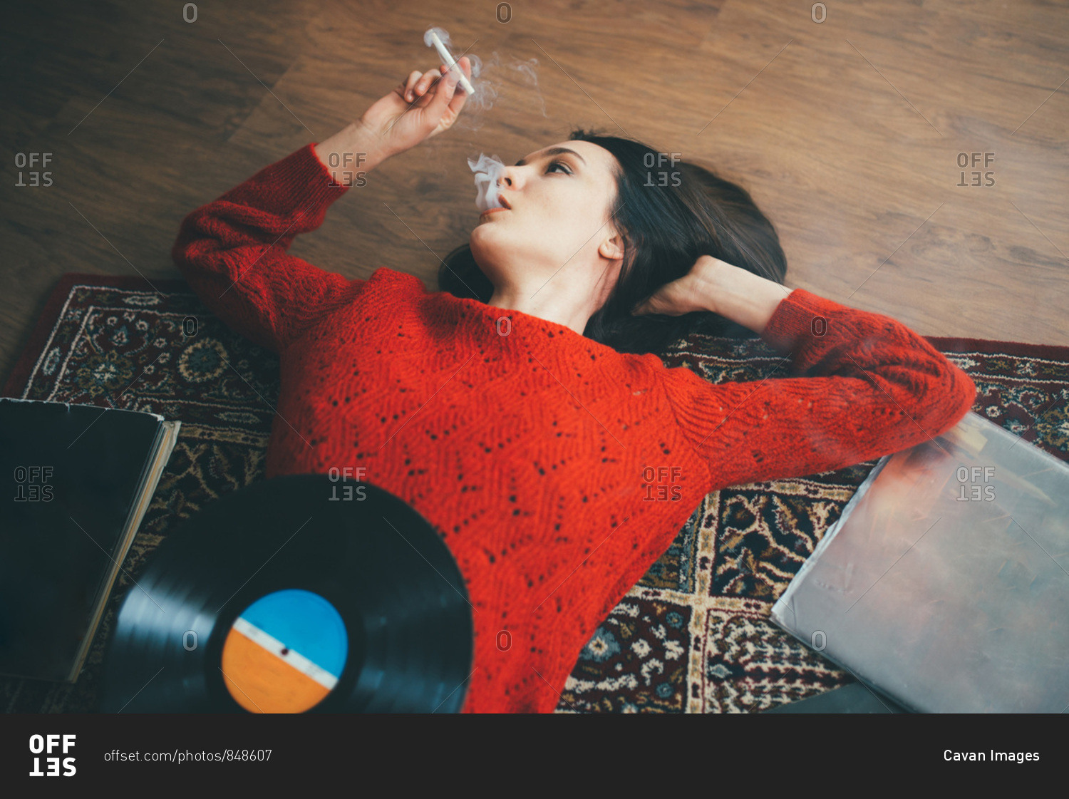 Woman lying on floor with vinyl, books and smoking cigarette. stock