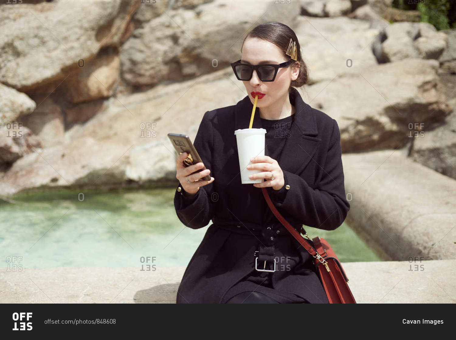 Young woman sitting by the fountain and drinking soda