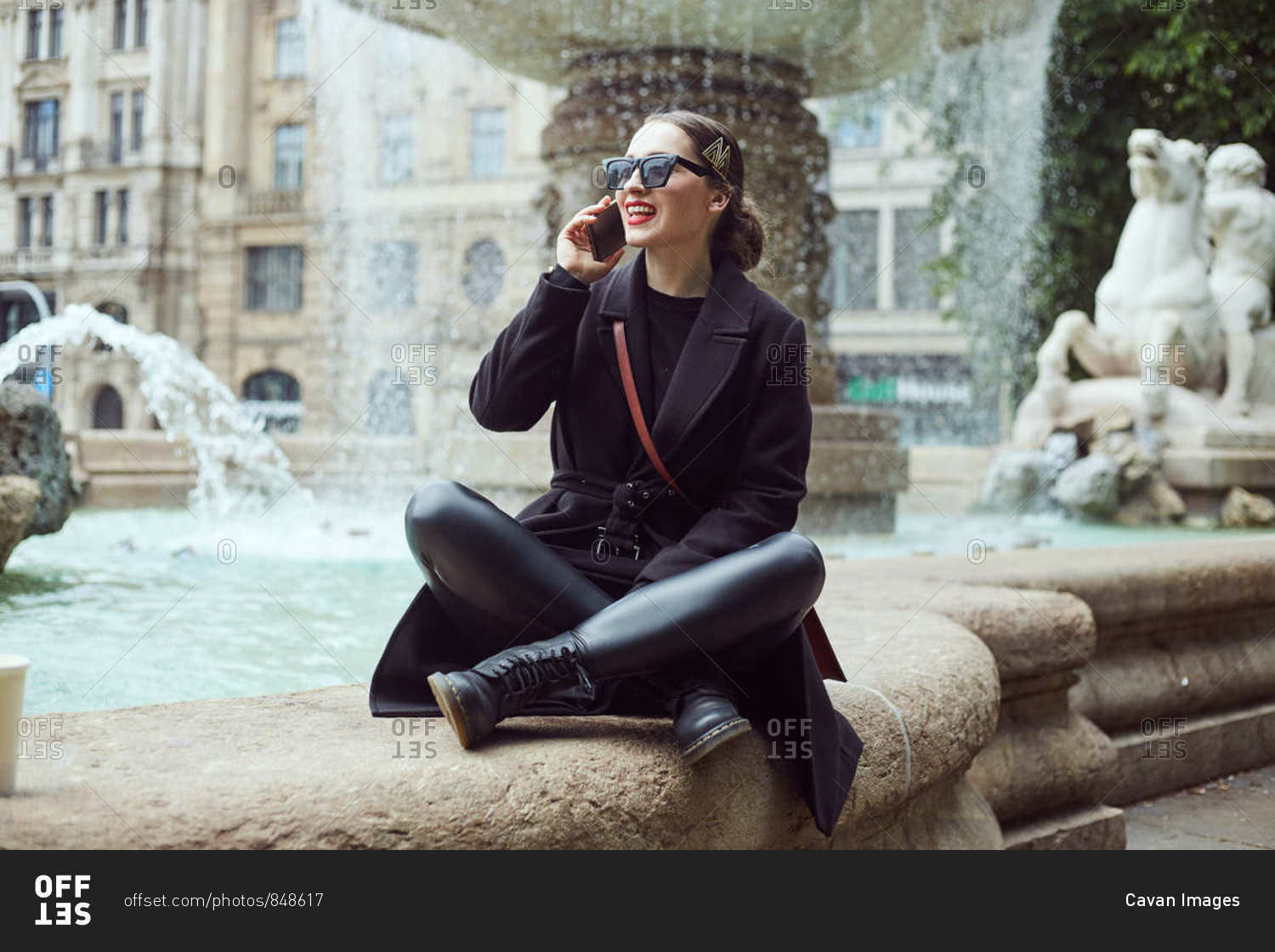 Young woman sitting by the fountain and talking on the phone
