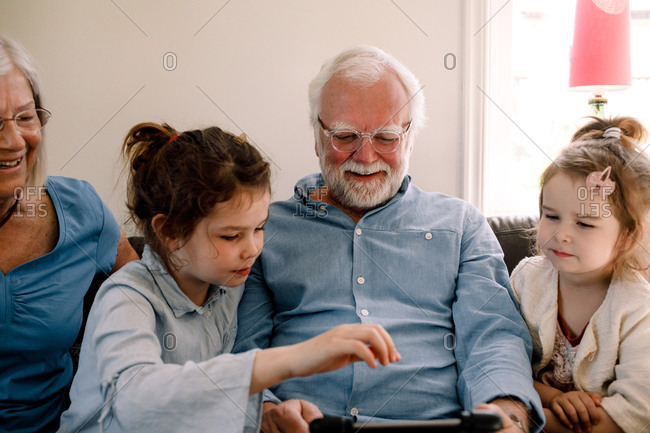 Smiling grandparents sitting with grandchildren while looking at digital tablet in living room at home