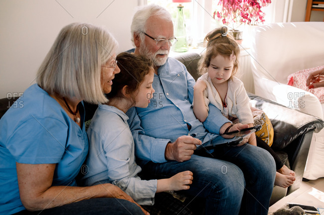 Grandparents and grandchildren using digital tablet while sitting in living room at home