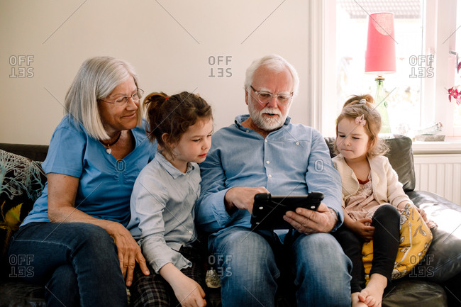 Grandparents sitting with grandchildren while using digital tablet in living room at home