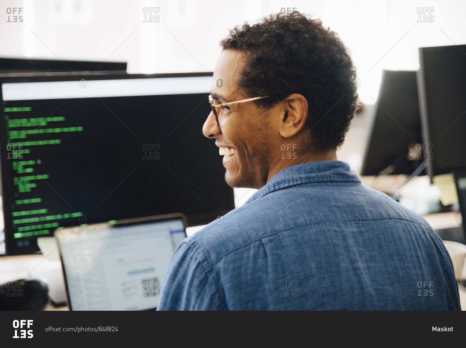 Rear view of cheerful male it professional looking away while sitting in creative office