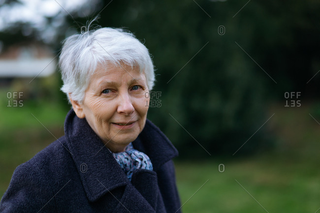 Mature woman posing in a garden in autumn, looking thoughtful and smiling