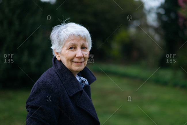 Mature woman standing in a garden in autumn, looking thoughtful and smiling