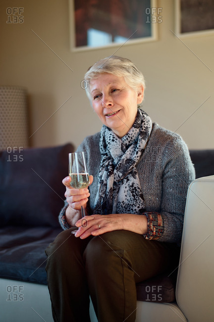 a mature woman sitting in a living room a glass of champagne in her hand looking smiling