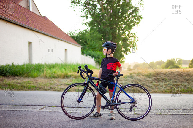 Young boy standing behind his road bike returning from a training session in the warm light of the end of the day