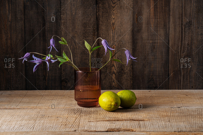 Purple flowers blossoming in a brown glass beside lemons