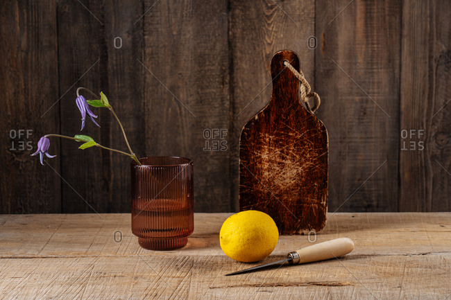 Lemon with knife on wooden surface by cutting board and purple flowers