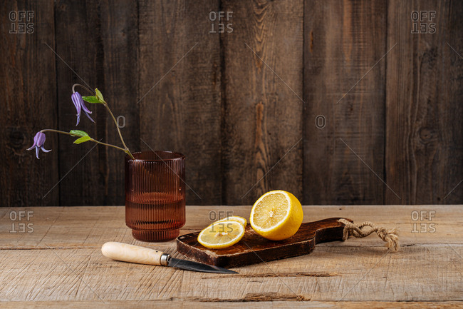 Lemon sliced on cutting board by glass with purple flowers