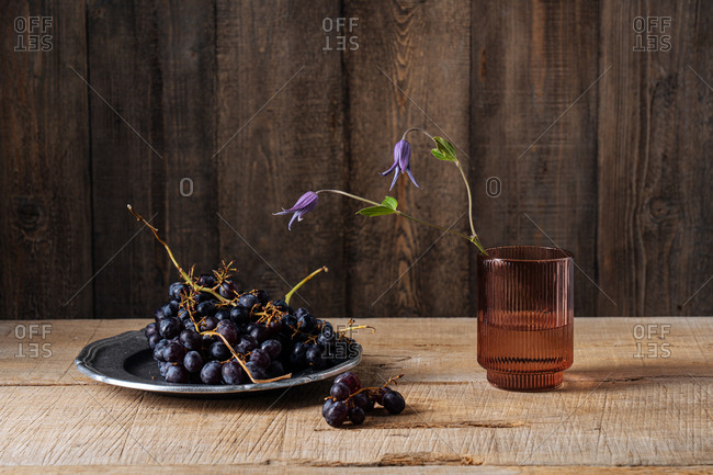 Purple flowers blossoming in a brown glass beside grapes