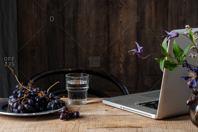 Grapes and flowers beside a laptop on wooden surface