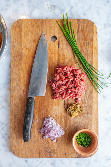 Overhead view of onion, chives and diced meat on a wooden cutting board